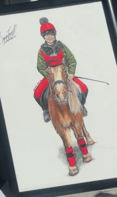 Framed portrait drawing of a boy in a red hat and green jacket riding a pony